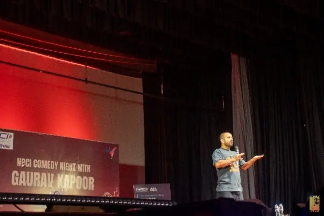 Gaurav Kapoor gesturing mid-set under red stage lights